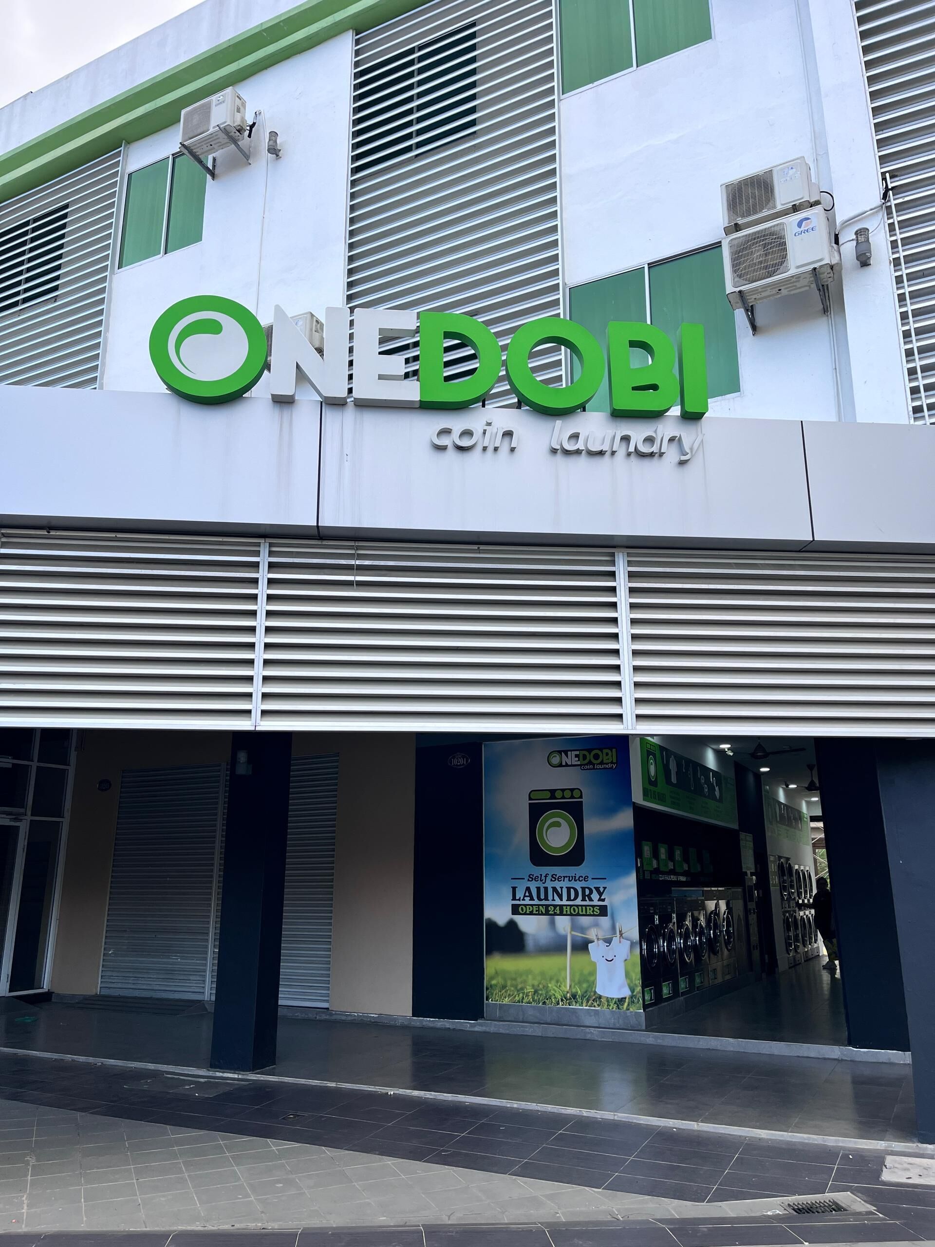 A building with a sign reading "ONE DOBI coin laundry" and an advertisement for self-service laundry open 24 hours.