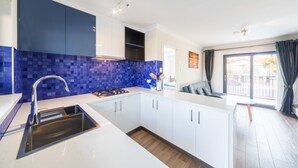 A modern kitchen with white cabinets, a blue tiled backsplash, and a built-in gas stove. - Batavia Apartment (Perth)