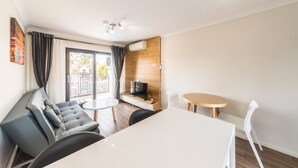 A modern living room with a sofa, a dining table, and a TV. - Batavia Apartment (Perth)