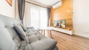 A modern living room with a grey sofa, a small white table, and a TV on a wooden wall. - Batavia Apartment (Perth)