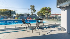 A poolside area with two metal chairs and a table, surrounded by a glass fence. - Batavia Apartment (Perth)