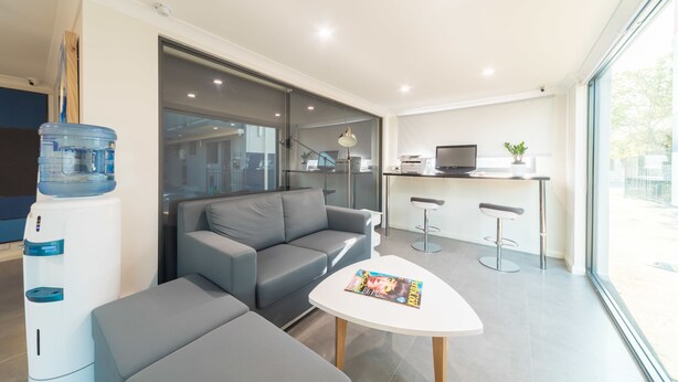 A modern living room with a grey sofa, a small table, and a water dispenser. - Batavia Apartment (Perth)