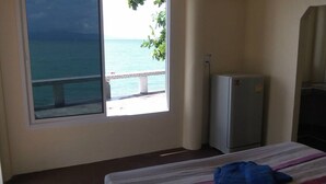 A room with a bed, a small refrigerator, and a window with a view of the sea and a pier. - Zen Zi Beach Rooms (Ko Pha-ngan)