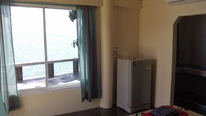 A room with a window overlooking a body of water, a small refrigerator, and a dark-colored cabinet. - Zen Zi Beach Rooms (Ko Pha-ngan)