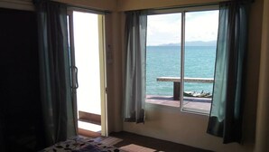 A room with a large sliding glass door leading to a balcony with a view of the sea and mountains. - Zen Zi Beach Rooms (Ko Pha-ngan)