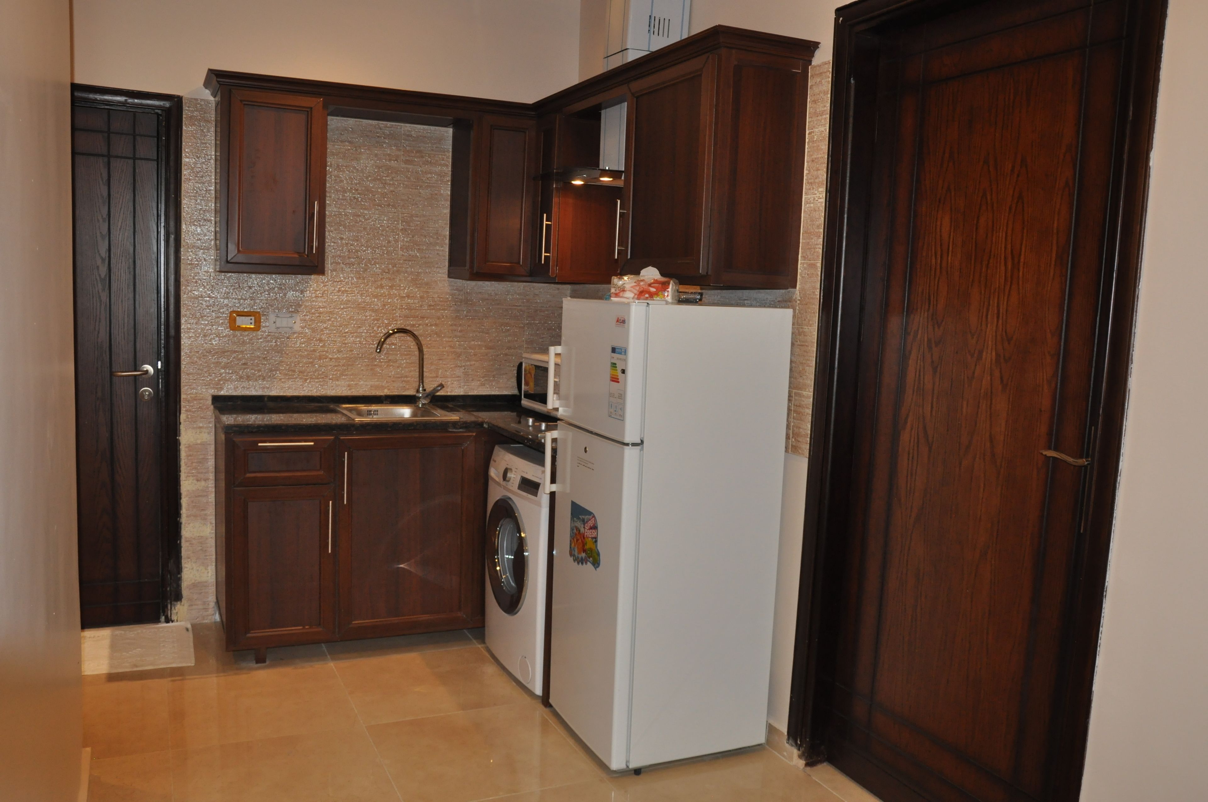 Una cocina compacta con armarios de madera oscura, lavadora y refrigerador.