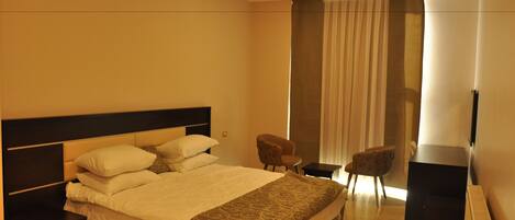 A hotel room with a large bed, a desk, a chair, a TV, and a window with curtains.