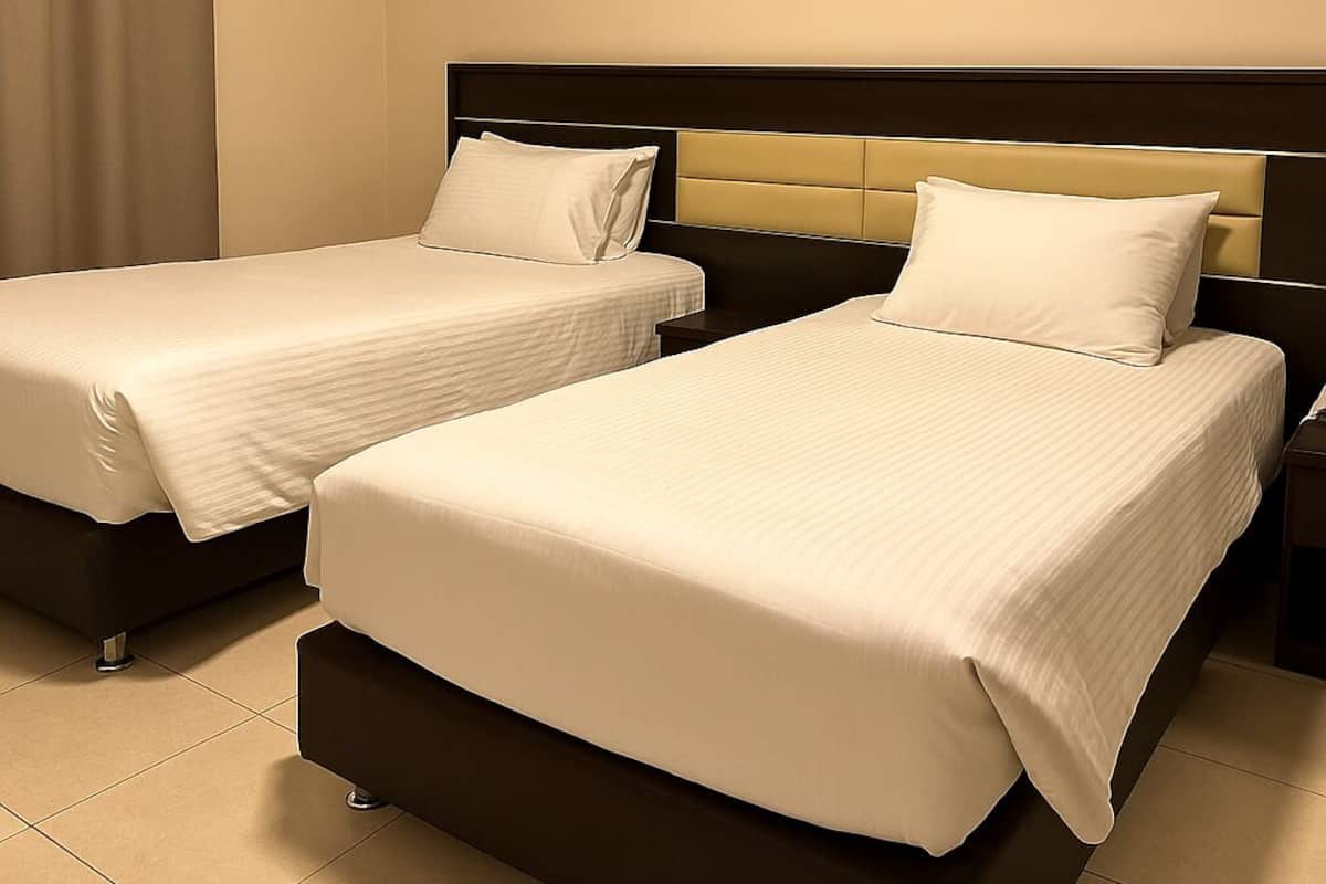 A hotel room with two beds, each with a headboard and pillows.