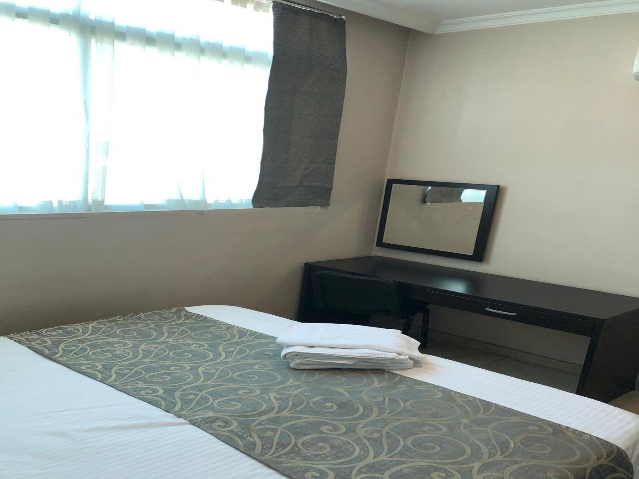 A hotel room with a bed, a desk, and a window with curtains.