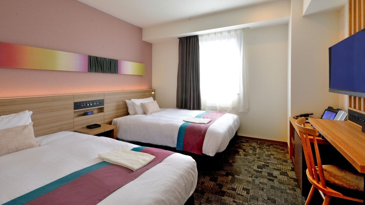 Une chambre d’hôtel avec deux lits, un bureau, une chaise, une télévision et une fenêtre avec des rideaux.