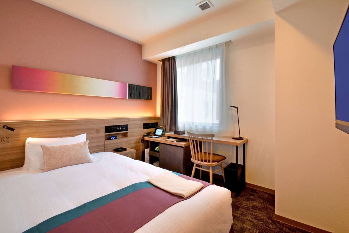 Ein Hotelzimmer mit Bett, Schreibtisch, Stuhl und einem großen Fenster mit Vorhängen.