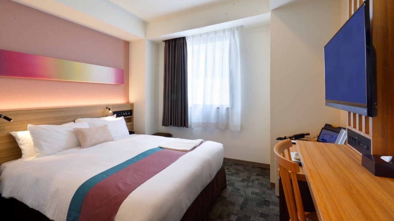 Une chambre d’hôtel avec un lit, un bureau, une télévision et une fenêtre avec des rideaux.