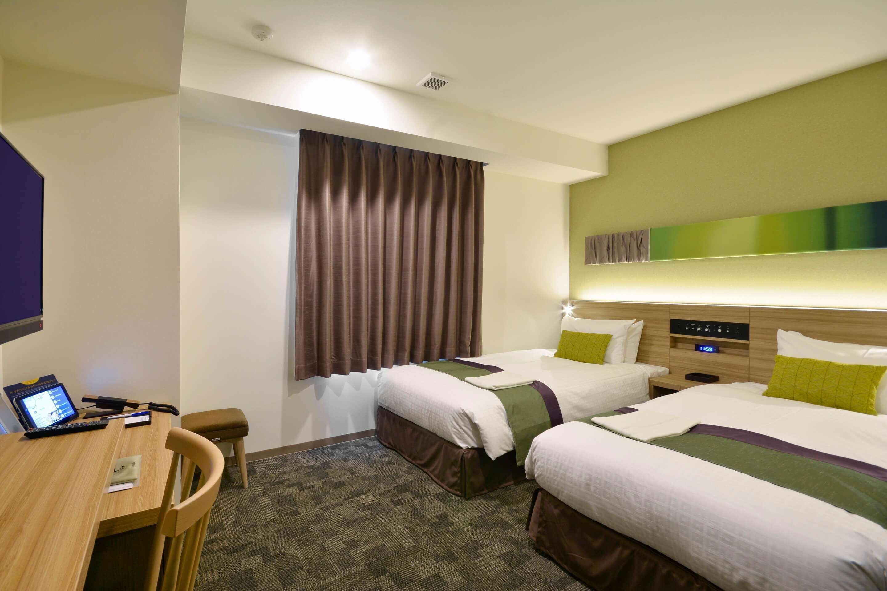 A hotel room with two beds, a desk, a chair, and a small table.