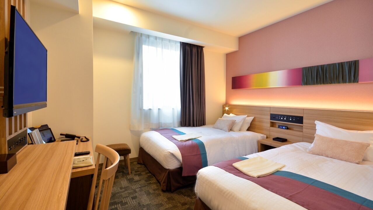 Une chambre d’hôtel avec deux lits, un bureau, une télévision et une fenêtre avec des rideaux.