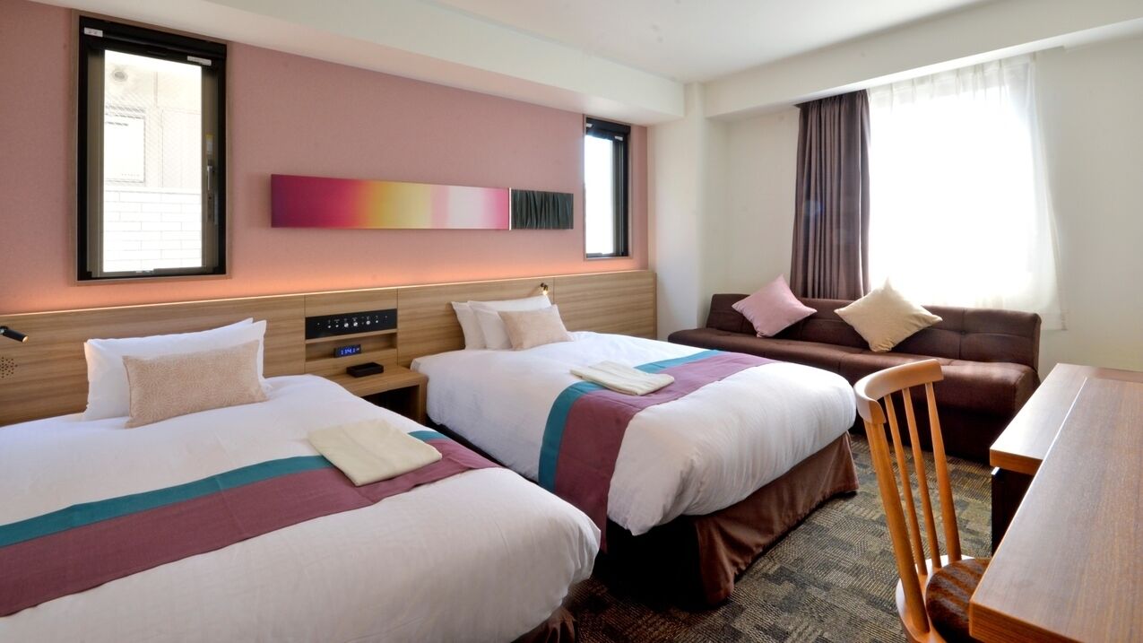 Une chambre d’hôtel avec deux lits, un canapé, une chaise en bois, un bureau et une fenêtre avec des rideaux.