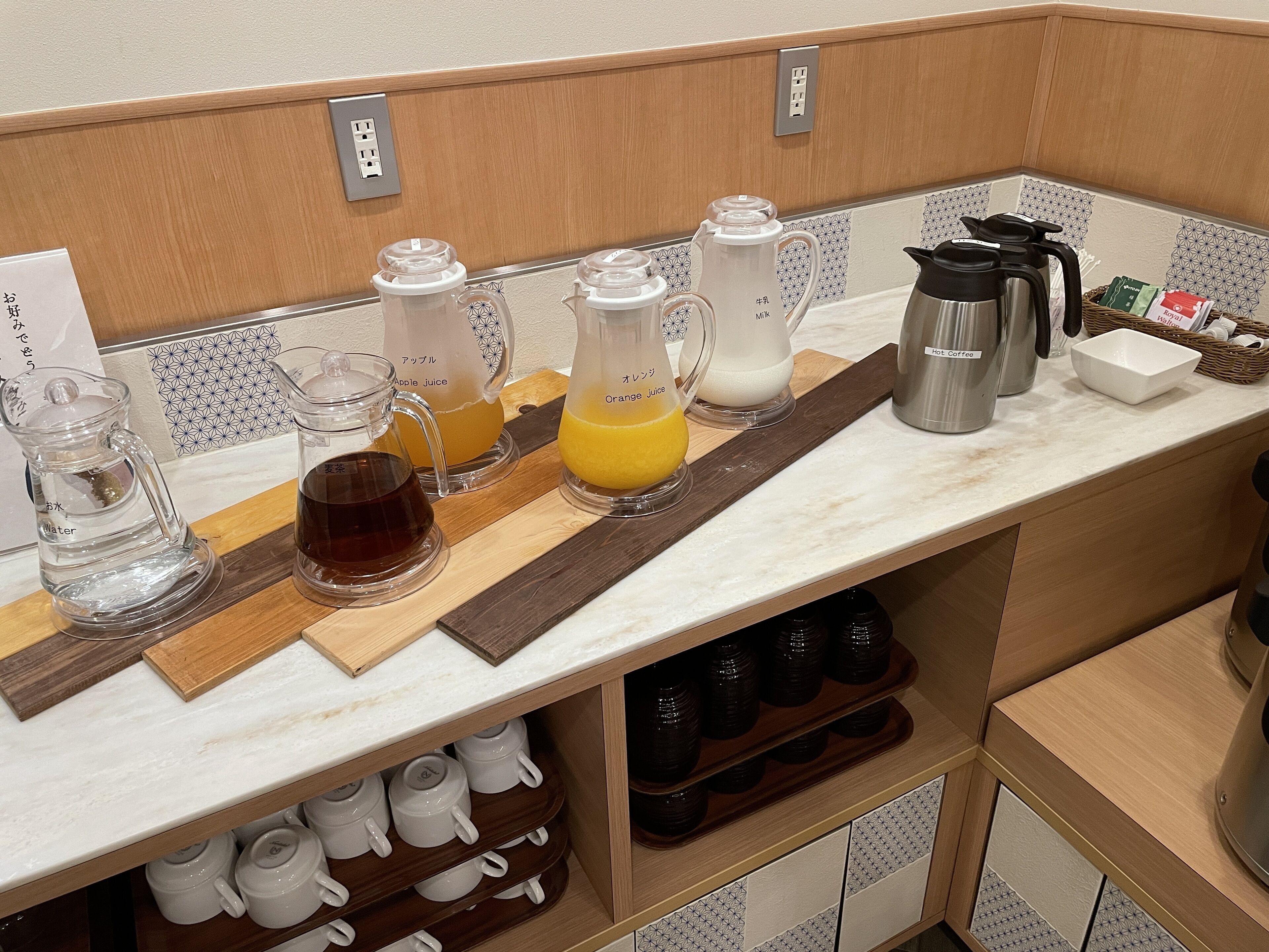 A kitchen counter with various appliances and containers, including a coffee maker, a kettle, and containers for apple and orange juice.