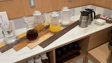A kitchen counter with various appliances and containers, including a coffee maker, a kettle, and containers for apple and orange juice.