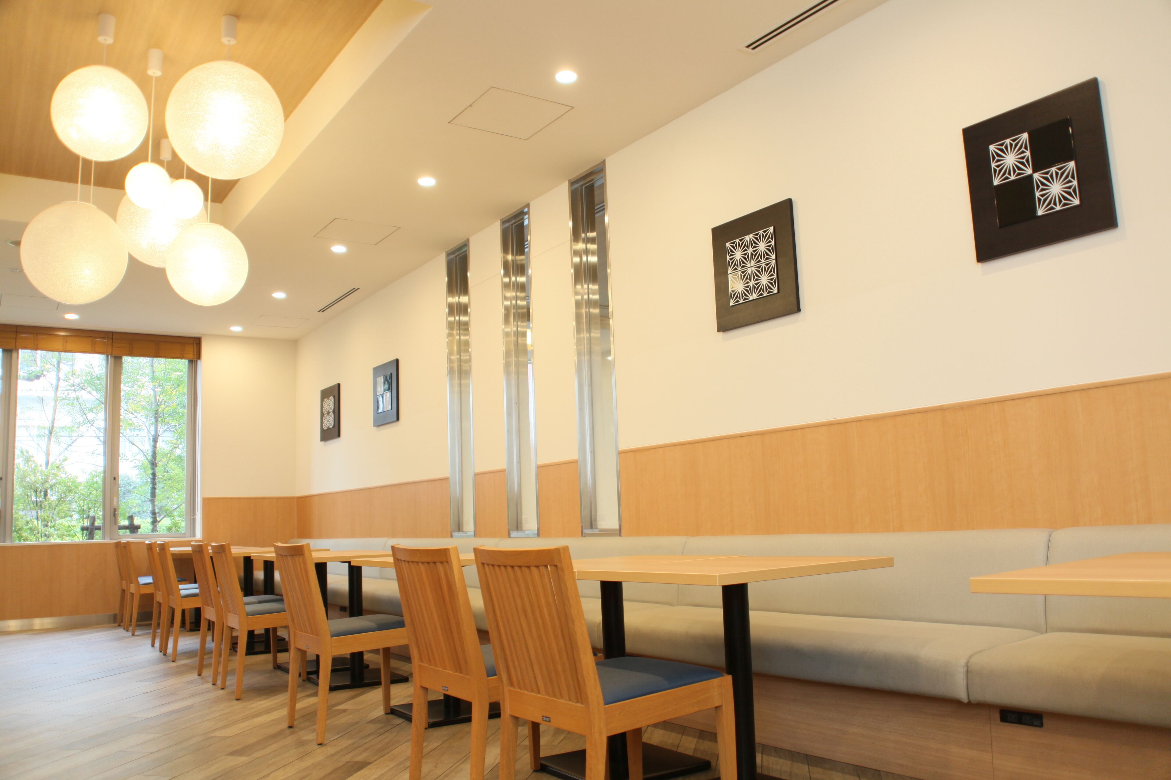 A modern dining area with wooden tables and chairs, large windows, and decorative wall art.