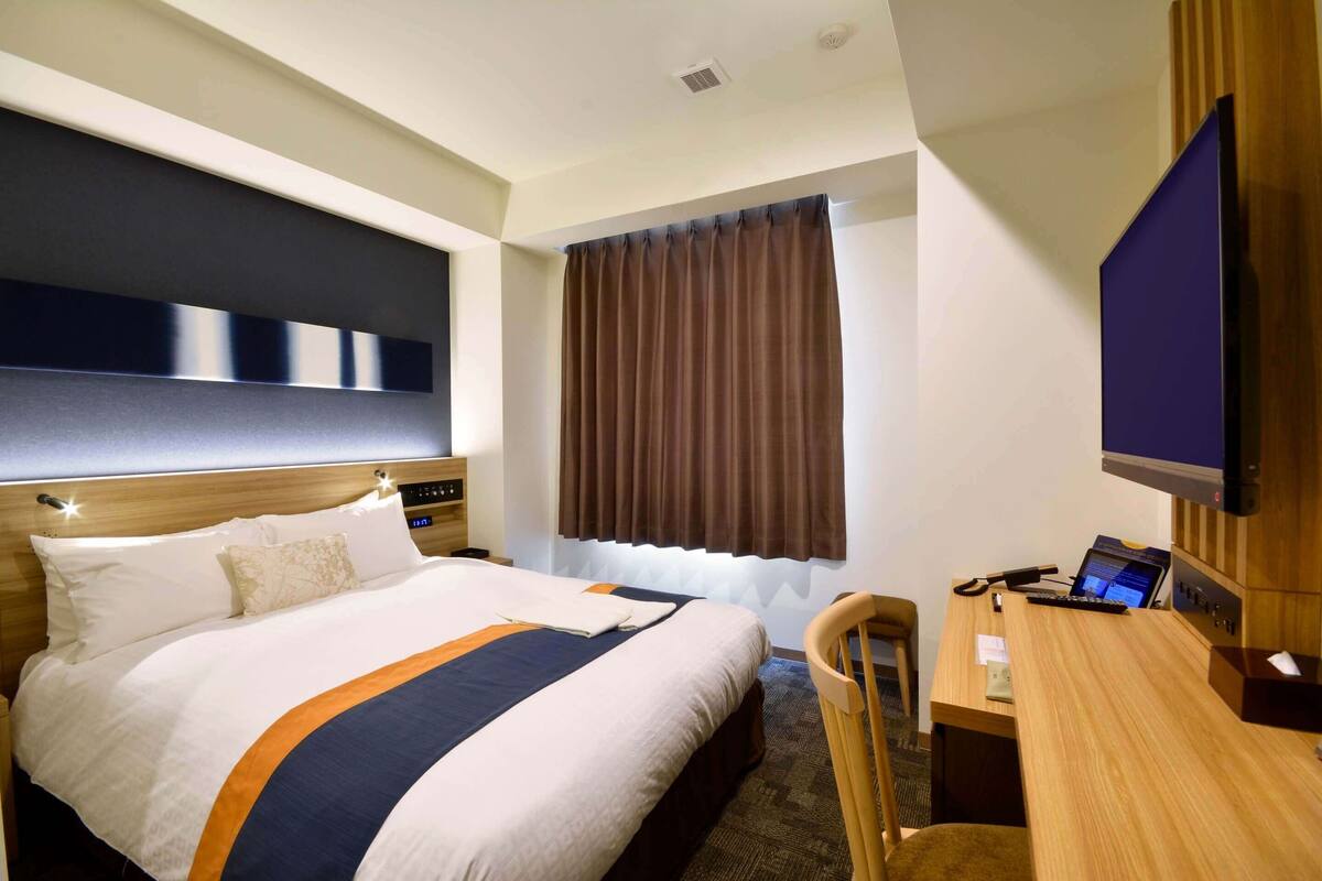 Ein Hotelzimmer mit einem großen Bett, einem Schreibtisch mit Computer und einem Fernseher.