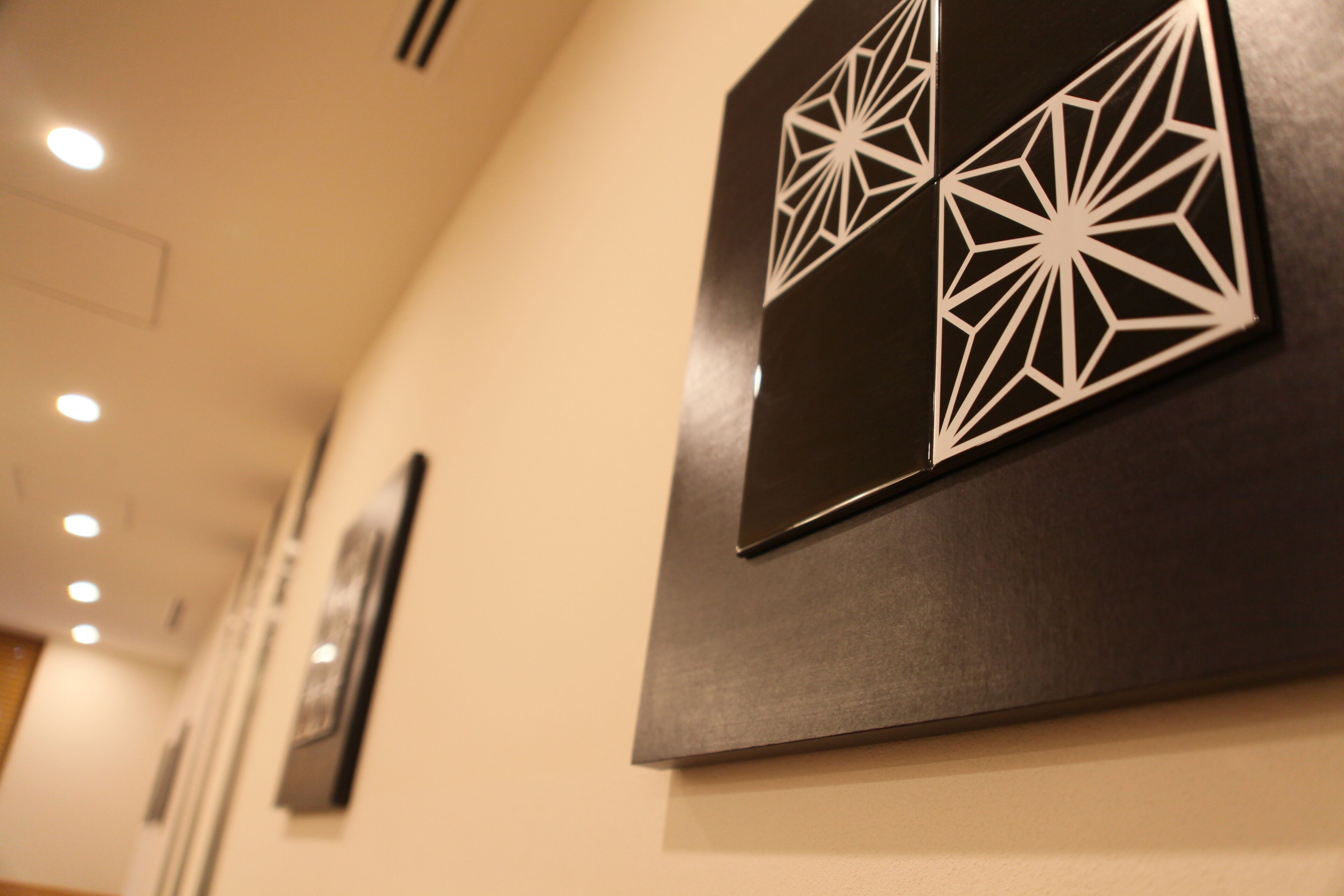 A corridor with wall-mounted geometric art pieces and recessed lighting.