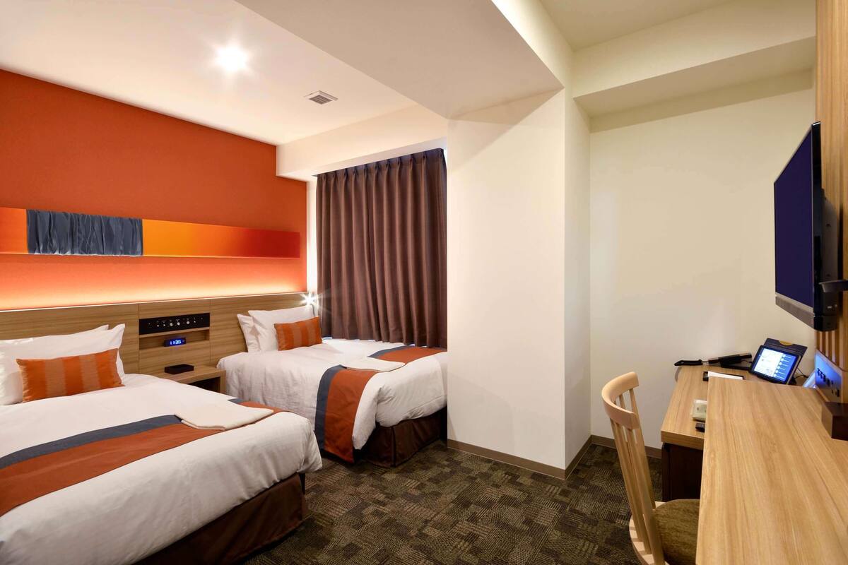 Ein Hotelzimmer mit zwei Betten, einem Schreibtisch, einem Stuhl, einem Fernseher und einer Steuerung.