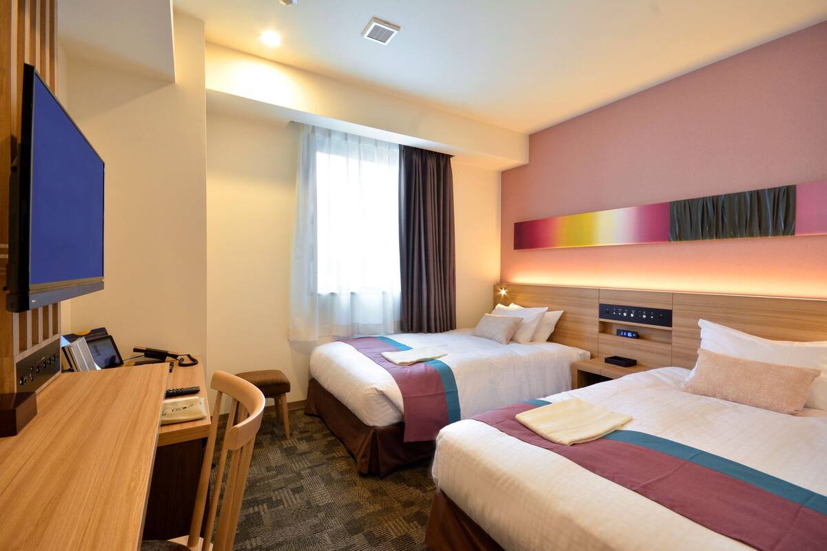 Ein Hotelzimmer mit zwei Betten, einem Schreibtisch und einem Fernseher.