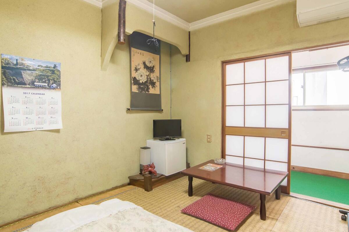 Une pièce traditionnelle japonaise avec un sol recouvert de tatamis, une porte coulissante en papier de riz (shoji), un téléviseur et un calendrier accroché au mur.