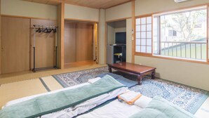 Une pièce de style japonais traditionnel, avec un sol recouvert de tatamis, un futon servant de lit, une table en bois, une télévision et un placard à portes coulissantes.