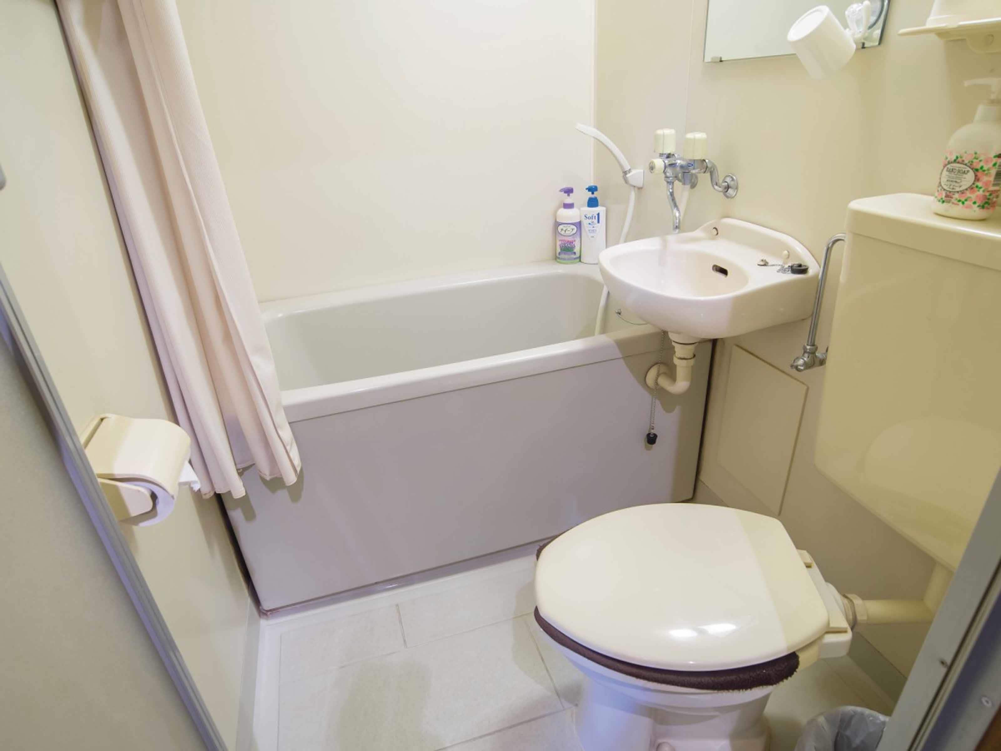 Een kleine badkamer met een bad, toilet en wastafel. Er staan toiletartikelen op de wastafel en een douchegordijn is gedeeltelijk open.