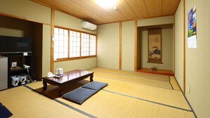 Une pièce de style japonais traditionnel, avec un sol recouvert de tatamis, une basse table en bois, un espace de sièges composé de tatamis, une porte coulissante et un climatiseur fixé au mur.