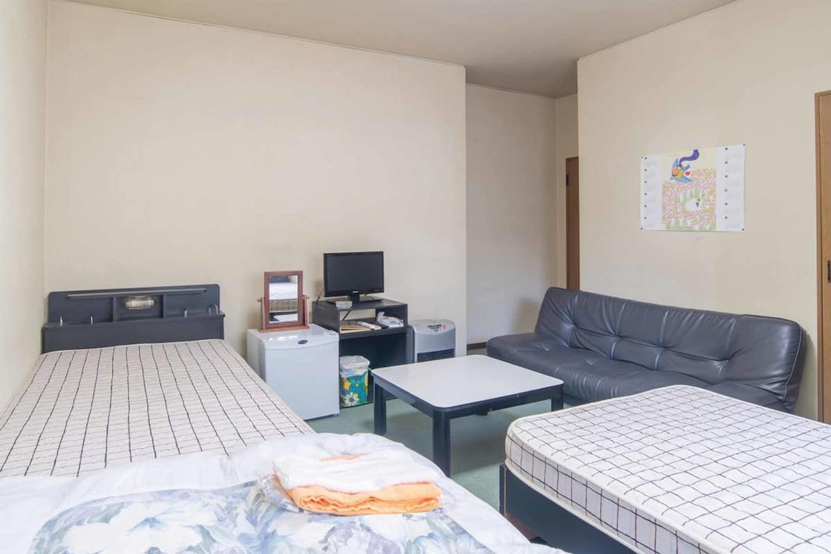 Une chambre d’hôtel avec un lit, un canapé, une petite table, une télévision et une affiche au mur.
