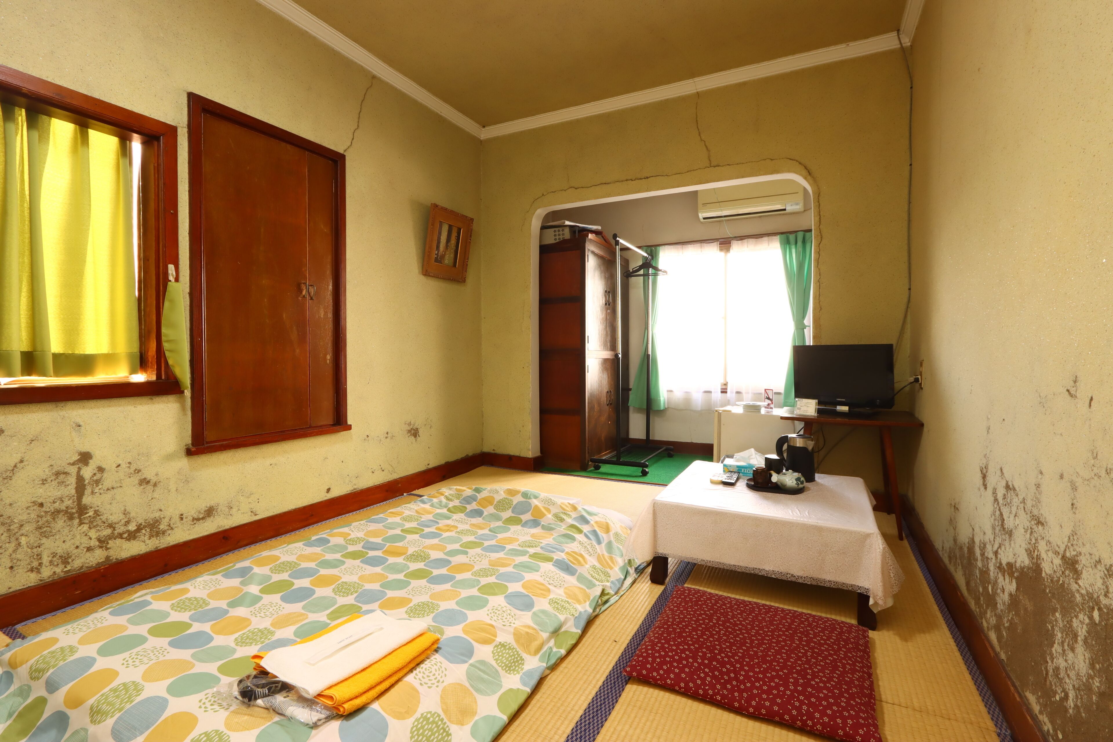Quarto com cama, uma mesinha com televisão e janela com cortinas.