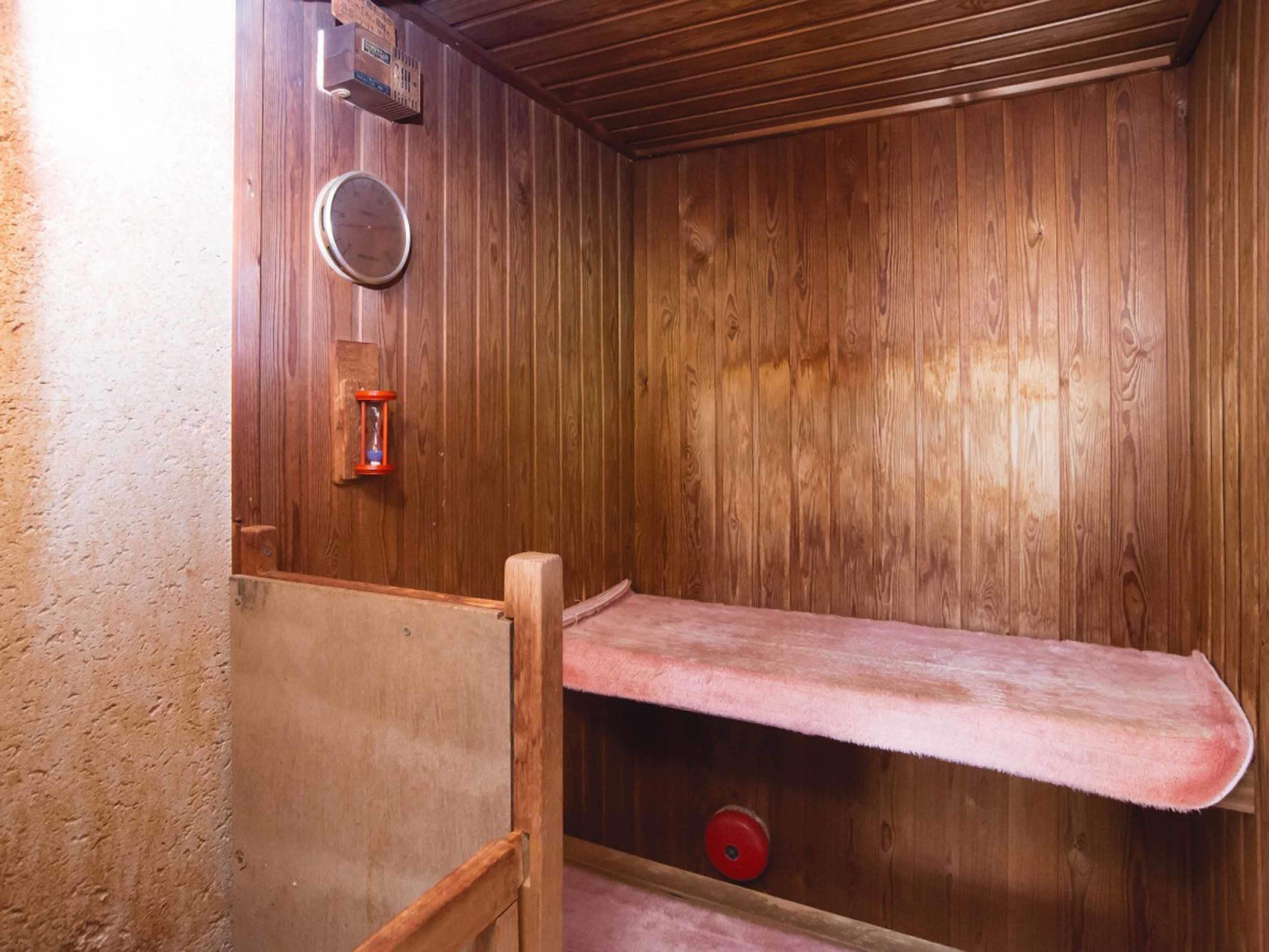 A wooden sauna with a bench, a wall-mounted heater, and a red wheel.