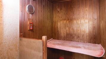 A wooden sauna with a bench, a wall-mounted heater, and a red wheel.