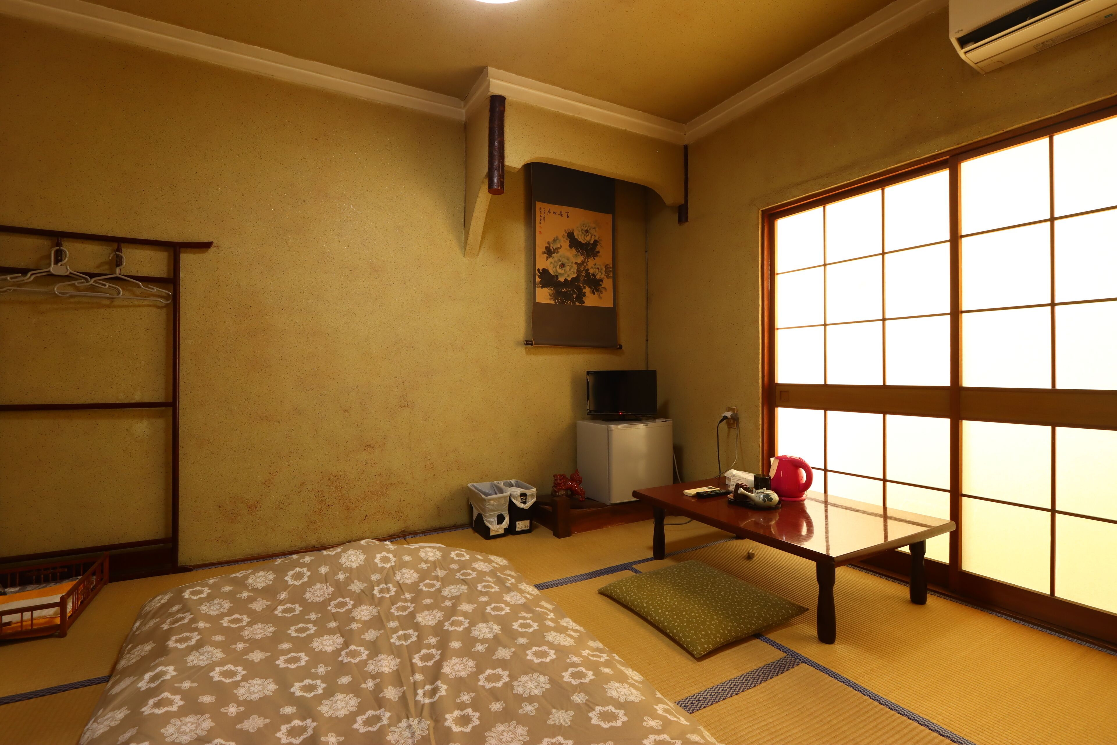 Una habitación tradicional japonesa con suelo de tatami, una cama futón, una mesita baja con un hervidor y una puerta corredera con diseño de cuadrícula.