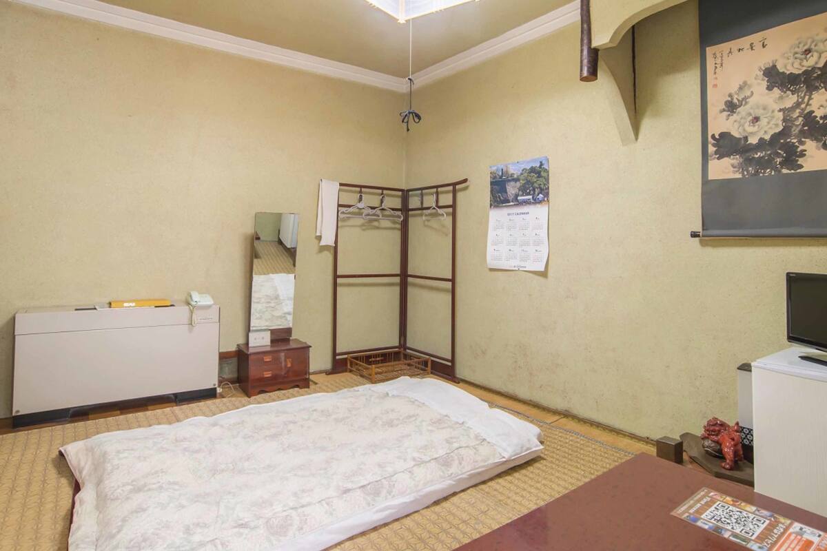 Une chambre d’hôtel comprenant un lit, une armoire, un bureau, un miroir, un calendrier et une petite statue.