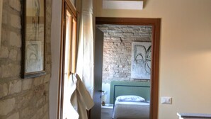 Un pasillo estrecho con techo de madera rústica, un radiador y una cama en la habitación contigua.