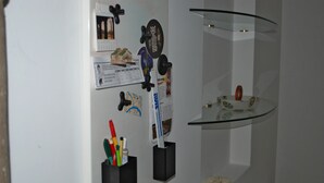 En vägg med olika föremål, inklusive en kalender, en affisch, en liten hylla med en dekorativ prydnad och en glashylla med ett litet föremål.