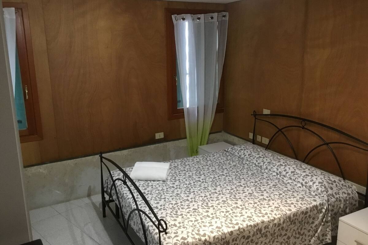 A bedroom with a bed, a window with curtains, and a wooden wall.