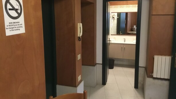 Un pasillo con un cartel de no fumar, un teléfono y un baño visible a través de una puerta abierta.