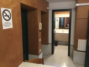 Un couloir avec un panneau indiquant qu'il est interdit de fumer, un téléphone et des toilettes visibles à travers une porte entrouverte.