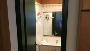 Un pasillo estrecho que conduce a un baño con lavamanos, espejo y perchero.