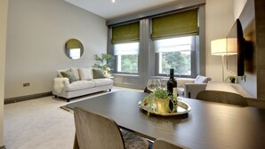 Uma sala de estar moderna com uma mesa de jantar, sofás e grandes janelas com persianas verdes.