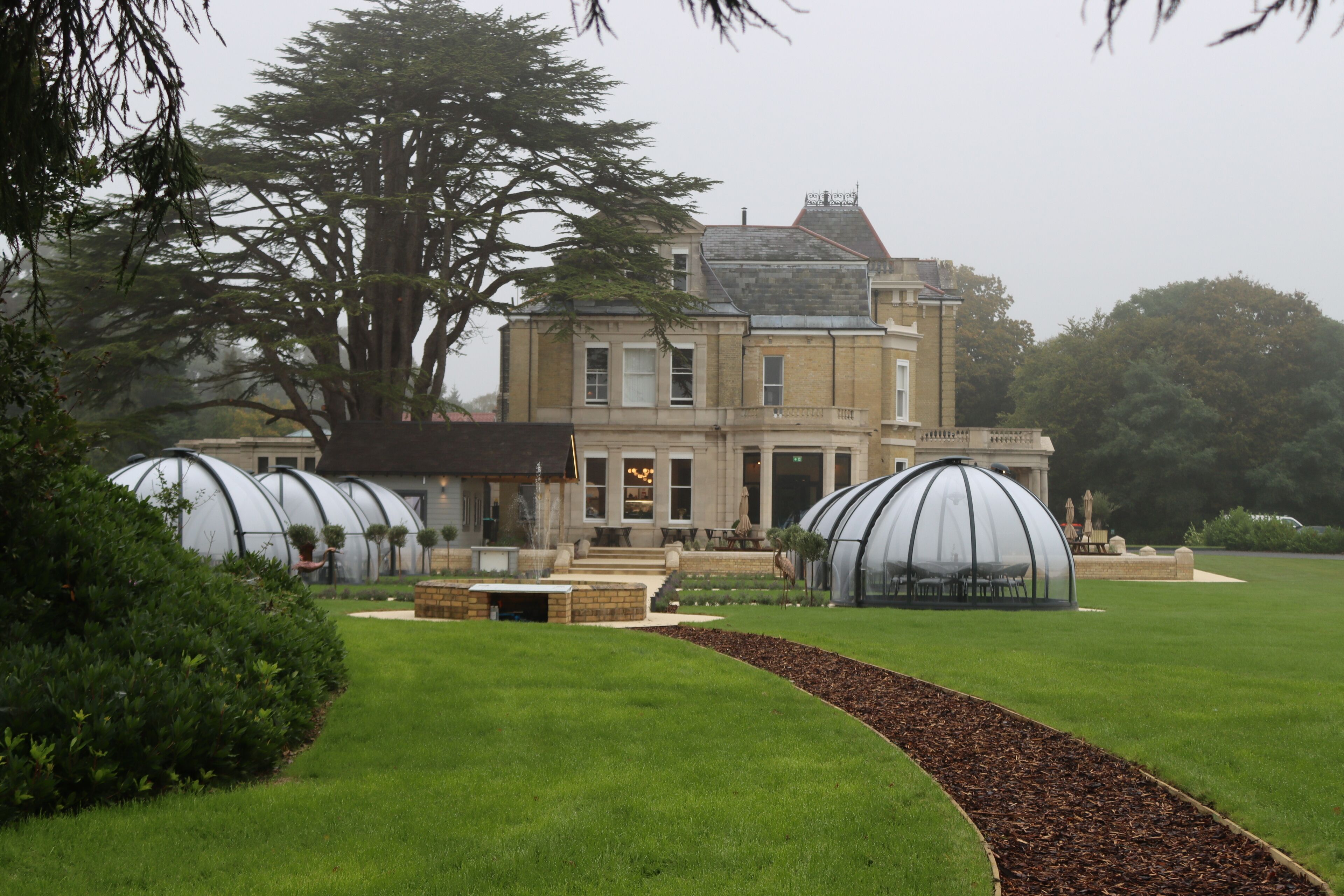A large building with a formal entrance, a lawn, and two large glass structures.