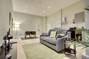 Una sala moderna con un sofá gris, una pequeña mesa de comedor y una alfombra verde.