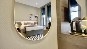 Quarto de hotel moderno com cama, mesa de cabeceira e TV de tela plana na parede.