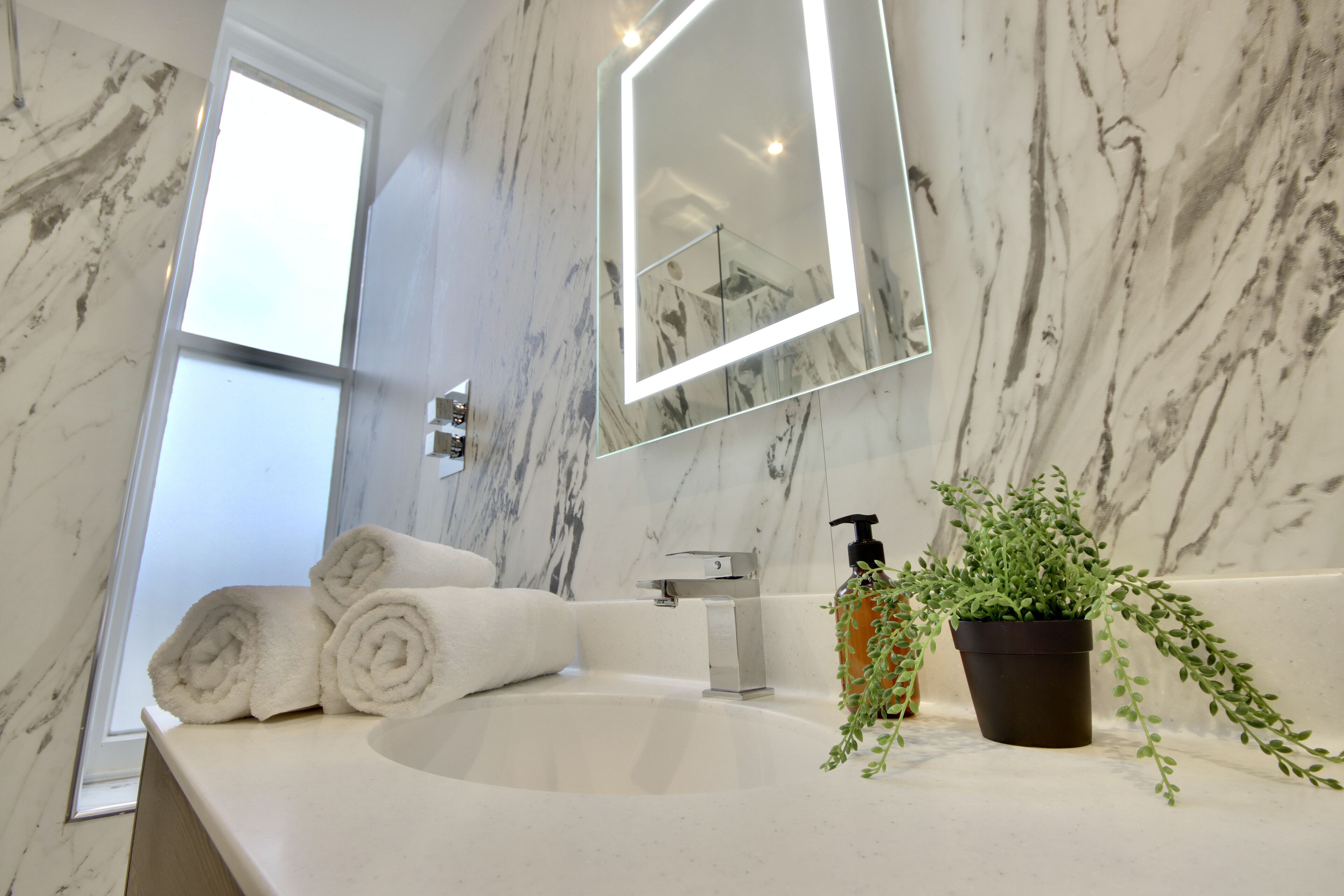 A bathroom with a marble sink, a large mirror, and a potted plant.