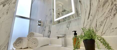 A bathroom with a marble sink, a large mirror, and a potted plant.