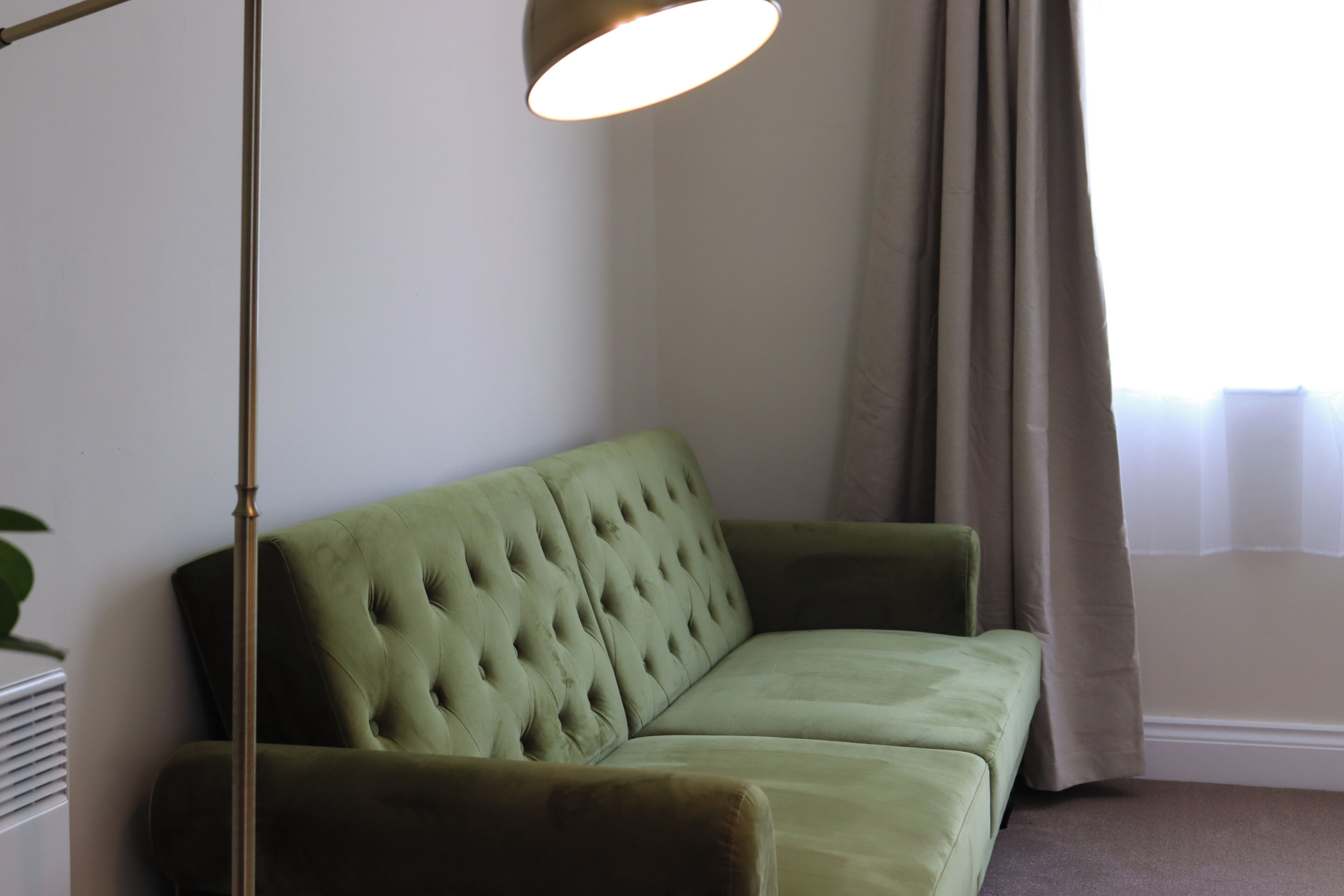 A green sofa in a room with a floor lamp and a window with curtains.