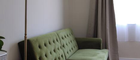 A green sofa in a room with a floor lamp and a window with curtains.